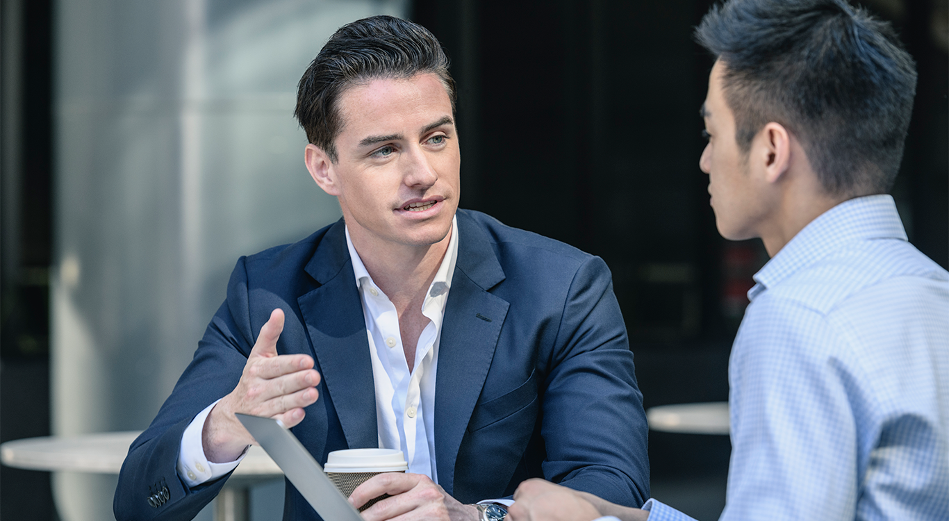 man speaking to another man who is working from a laptop